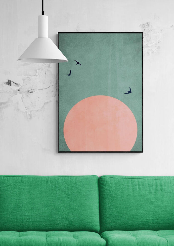 Framed "A Beautiful Day" by Boris Draschoff above a green sofa, featuring a pink sun and flying birds.