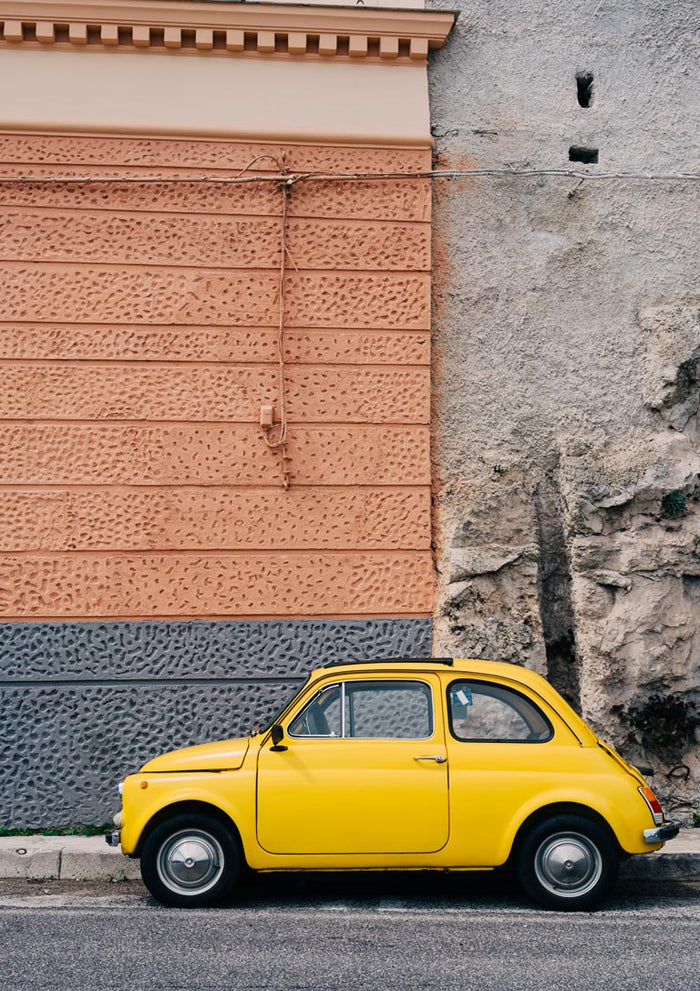 A yellow vintage car parked beside a textured wall on the Amalfi Coast Drive XII.