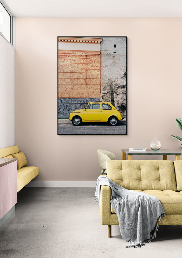 Framed print of a yellow car on the Amalfi Coast displayed above a beige sofa in a modern living room.