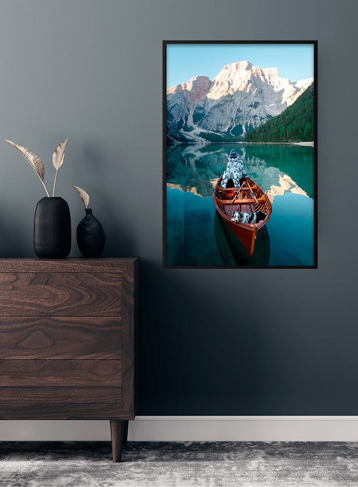 Framed poster of an astronaut in a canoe on a serene lake with mountains, displayed above a wooden dresser.