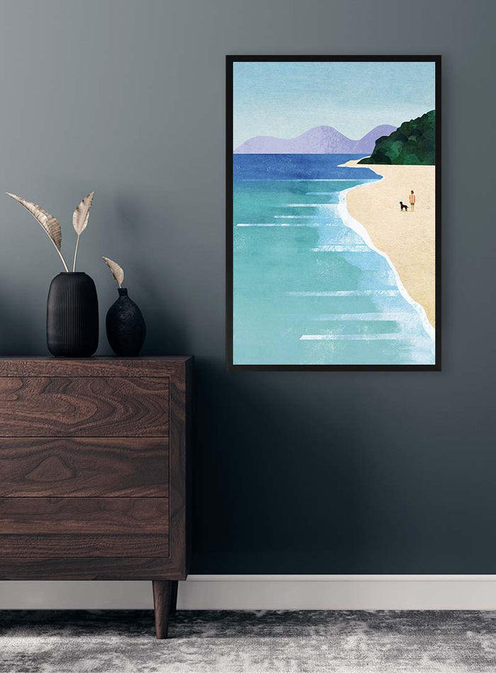 Framed Beach Girl II by Henry Rivers above a wooden dresser, featuring a serene beach with distant mountains.