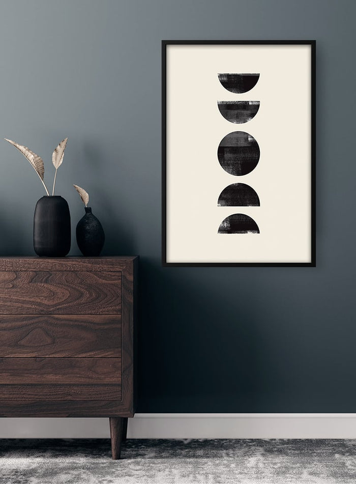 Black Circles Plakat artwork with four black semicircles, framed and hung on a dark wall above a wooden dresser.
