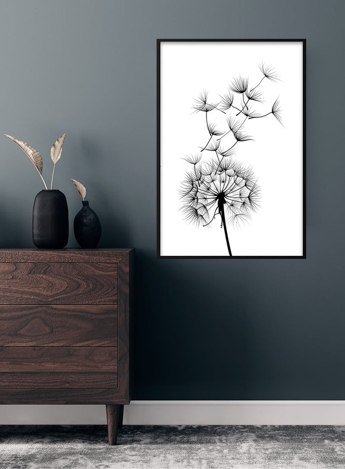 Minimalist black dandelion flower poster in a frame, displayed above a wooden dresser against a grey wall.