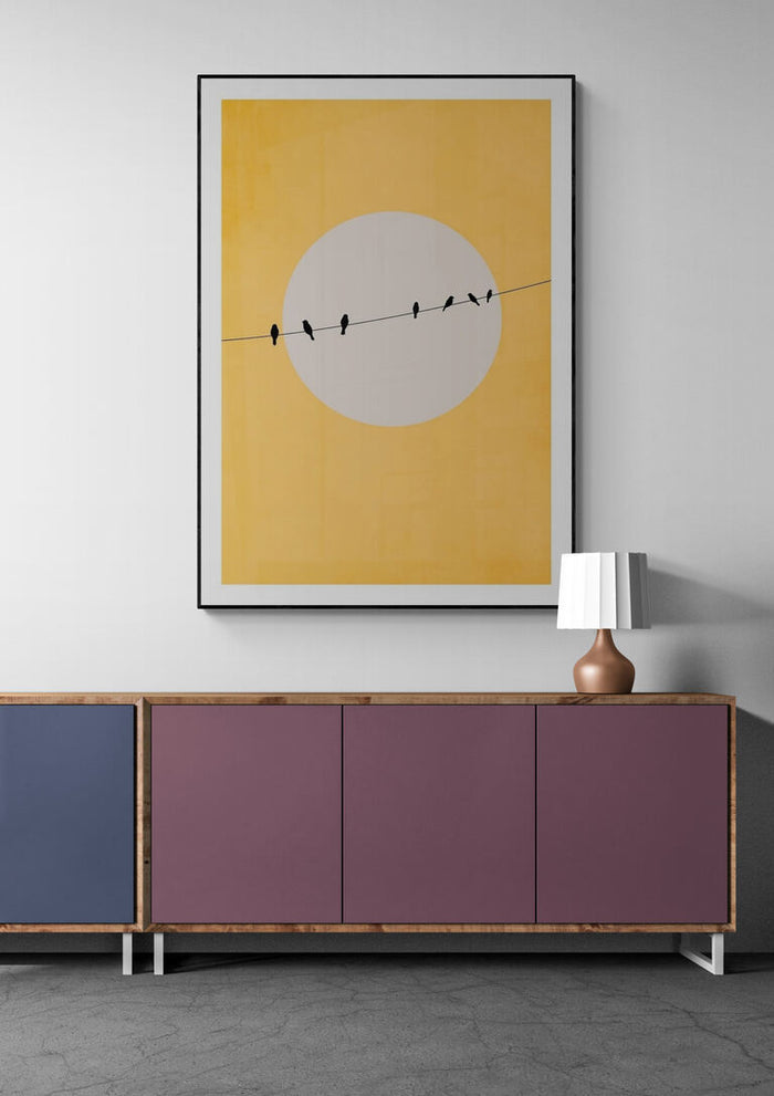 Chirping and Chilling - Boris Draschoff artwork of birds on a wire against a yellow sun, framed above modern credenza.