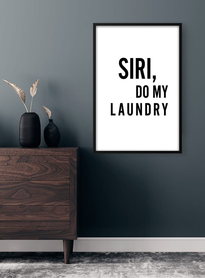 Minimalist poster on wall with text "Siri, do my laundry" above a wooden dresser in modern room.