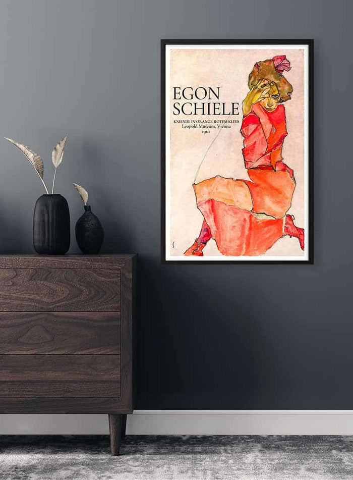Framed Egon Schiele - Kniende in orange-rotem Kleid, 1910 poster on a dark wall above a wooden dresser.