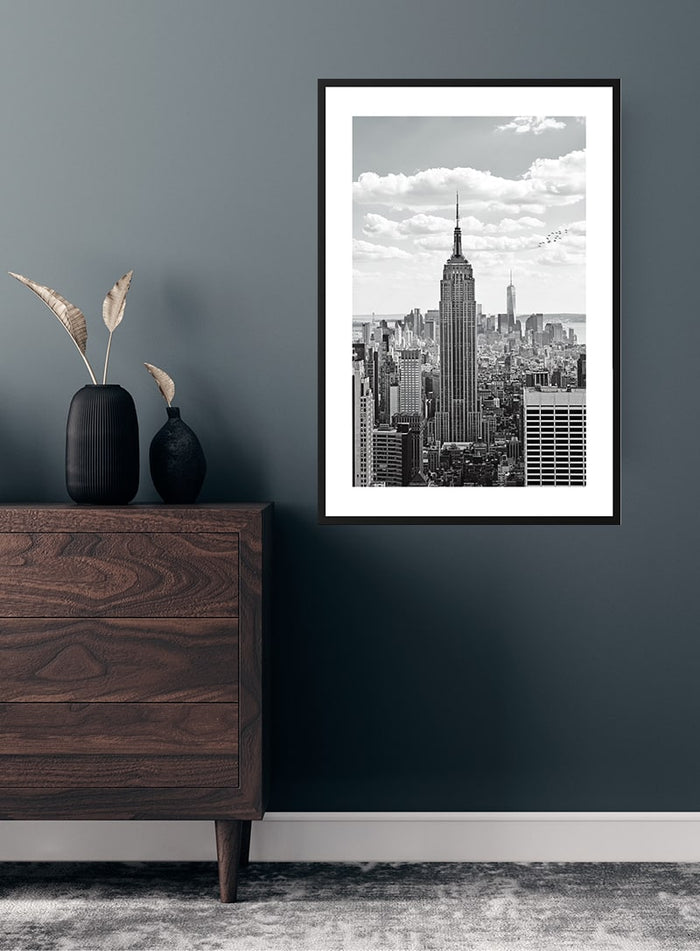 Empire State Building poster in a modern room setting, displayed above a wooden dresser against a dark wall.