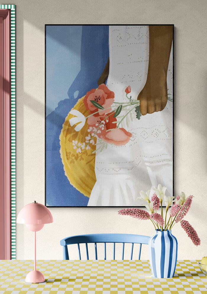 Art print of a hand holding pink flowers, hung above a table with a striped vase and pastel decor.