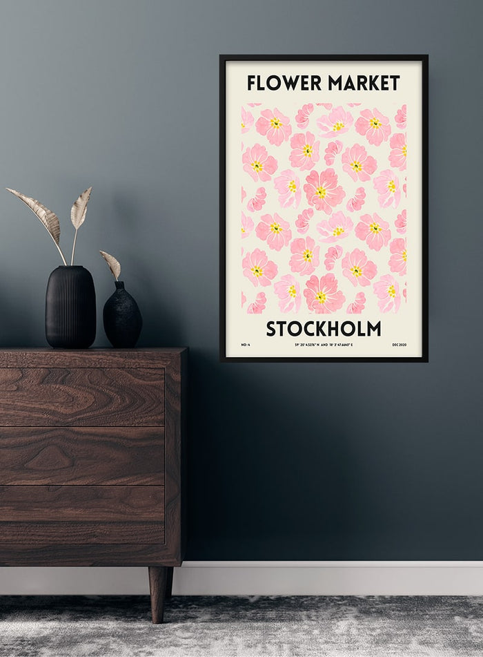 Flower Market - Stockholm poster featuring pink flowers, framed and hung on a dark wall above a wooden cabinet.