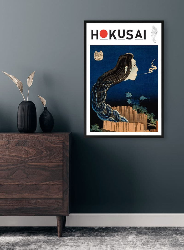 Framed print of Katsushika Hokusai's "The Plate Mansion" displayed on a dark wall above a wooden dresser.
