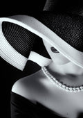 Black and white portrait of a woman in a wide-brim hat, pearl necklace, and off-shoulder dress.