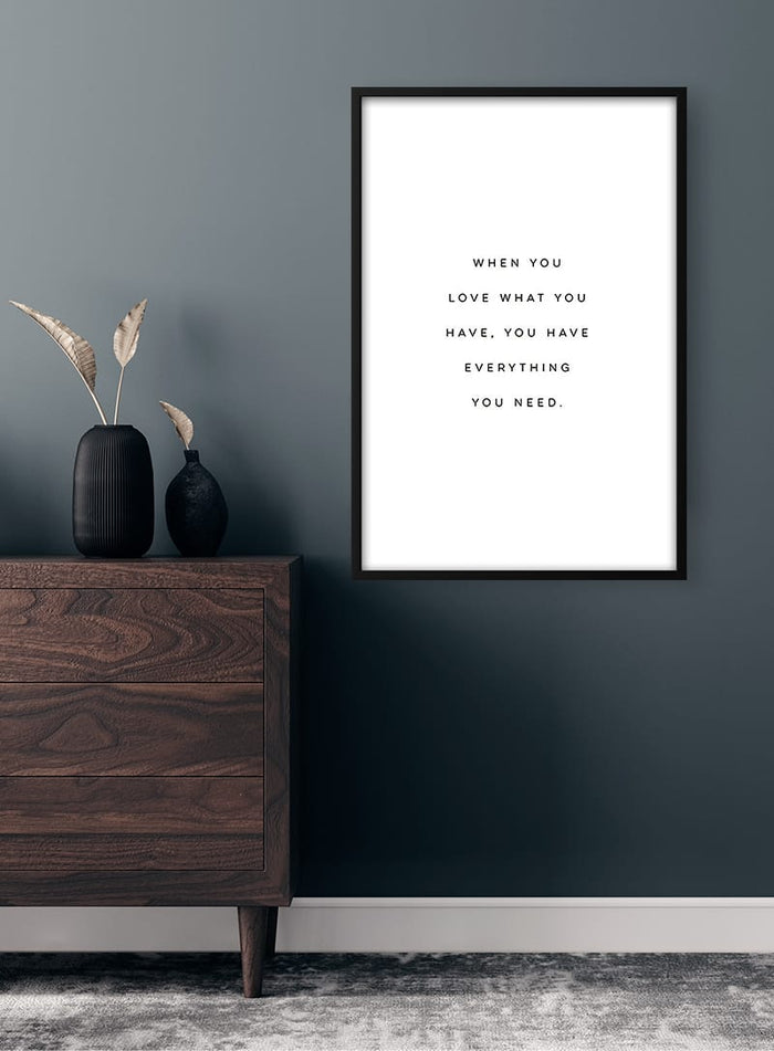 Minimalist "Love What You Have" quote poster in a black frame on a dark wall above wooden dresser.