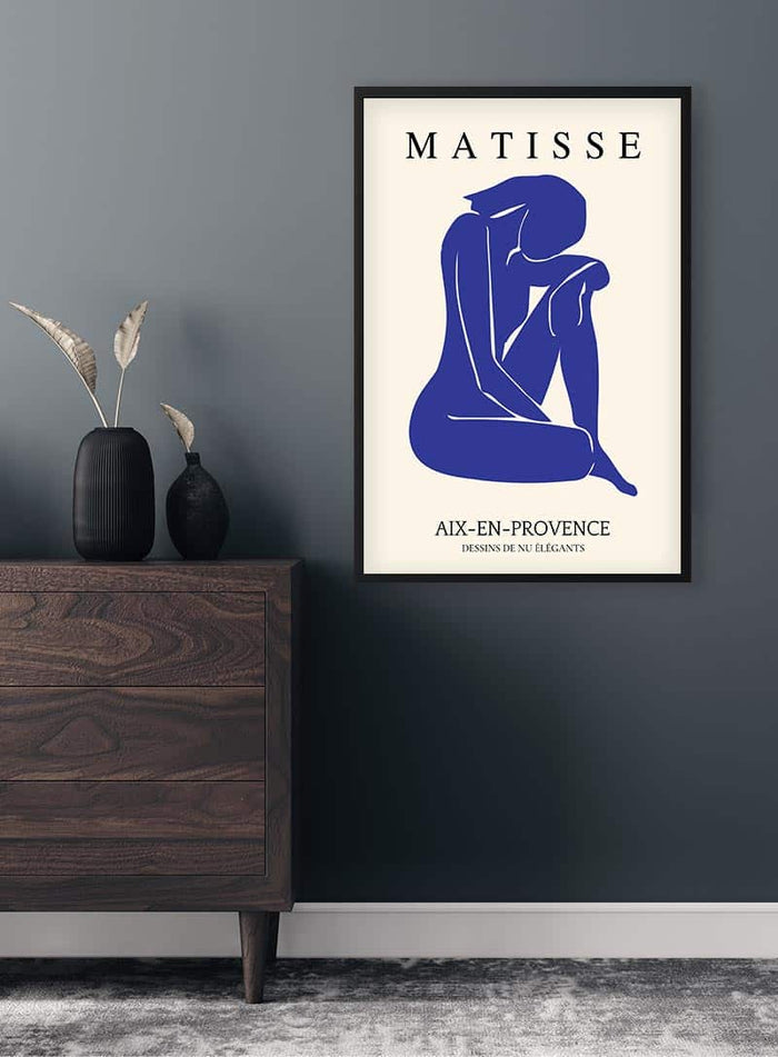 Framed Matisse inspired blue cutout poster of a seated figure, displayed on a wall above a modern dresser.