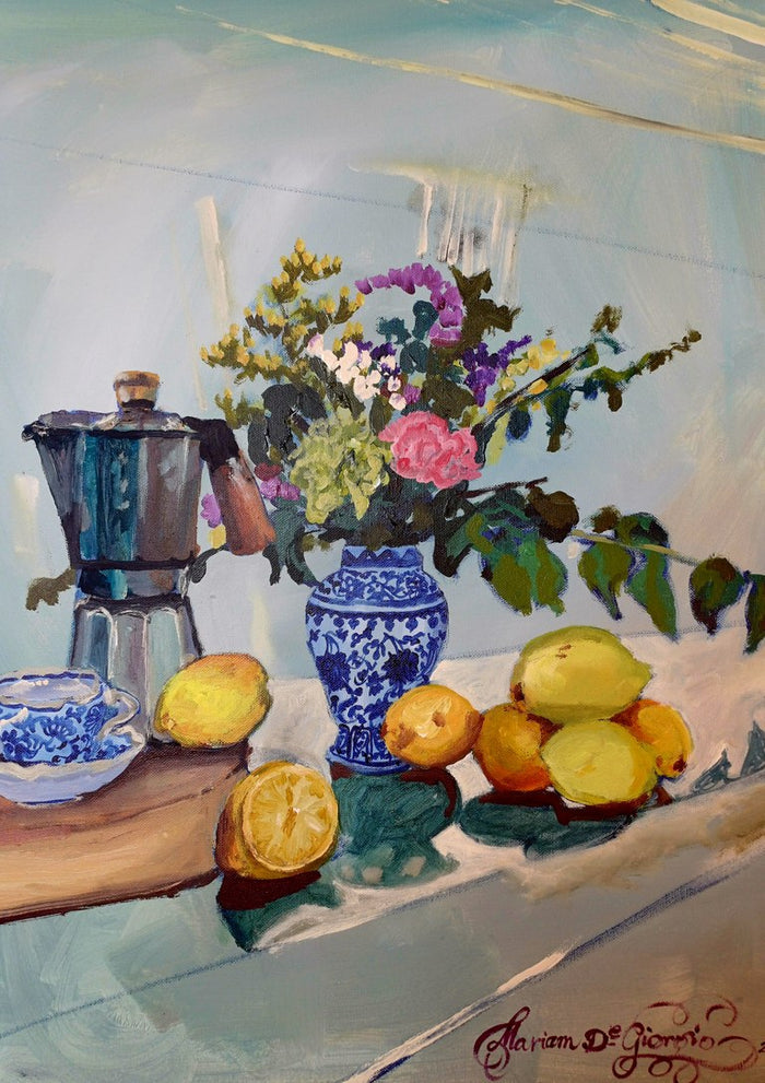 Morning coffee by Mariam De Giorgio — a steel espresso pot, lemons and a blue-and-white vase of flowers on a pale table.
