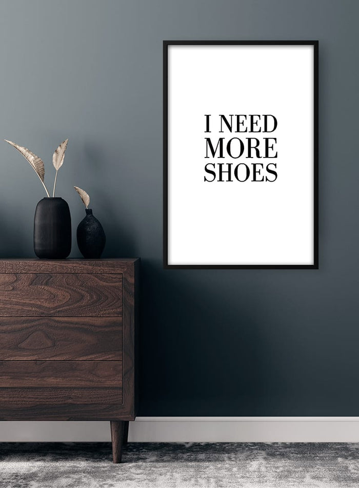 Minimalist "I Need More Shoes" poster in black frame, styled above a wooden dresser in a modern room.