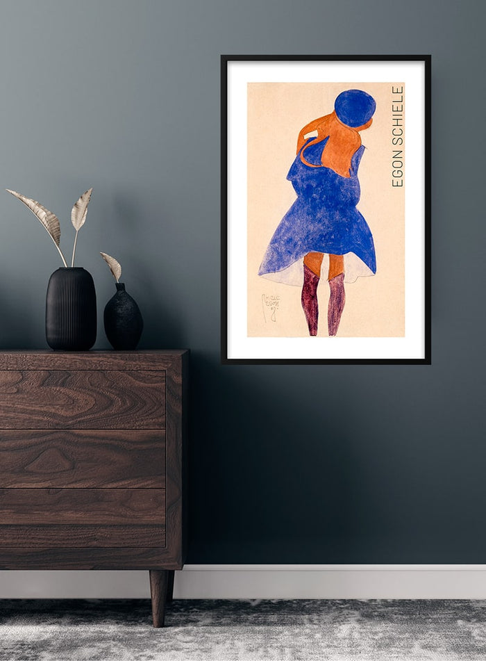 Framed art print of Egon Schiele's "Standing Girl, Back View (1908)" displayed on a dark wall above a wooden dresser.