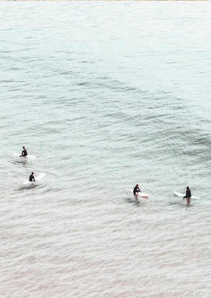 Four surfers on surfboards sit in calm, pale water seen from above for Surfers in Water Plakat.