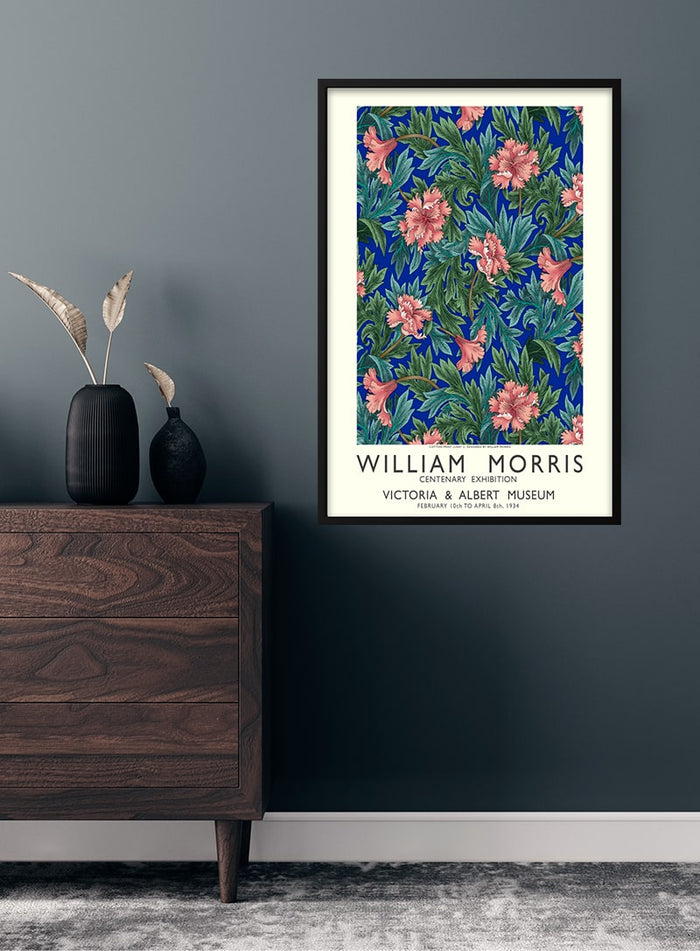 Framed William Morris flower exhibition poster with intricate floral design on a dark wall above a wooden dresser.
