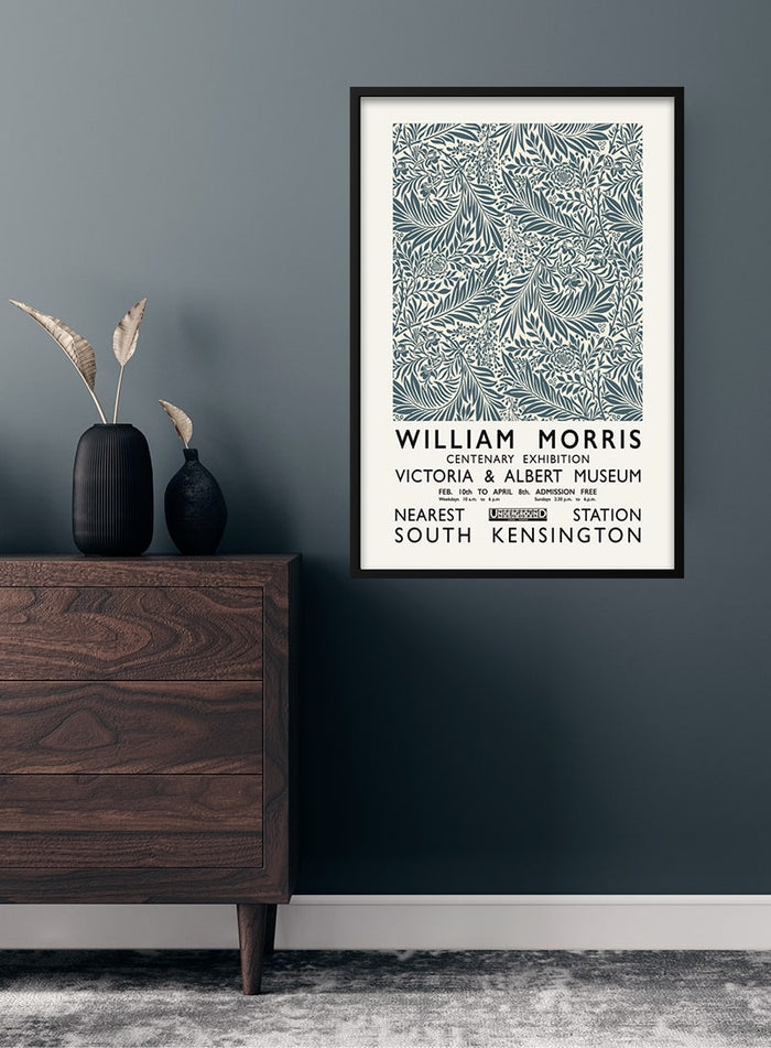Framed William Morris grey poster with botanical design hanging on a dark wall above a wooden dresser.